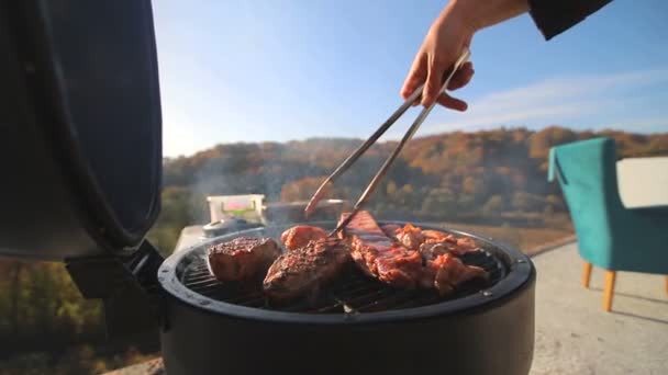 肉、鶏肉、リブ、火の上で揚げた作品。シェフの手が肉をめくる。美しいパノラマに対して、家の屋根の上でBbq肉を調理します. — ストック動画