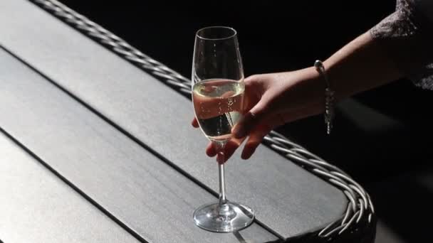 La suave mano femenina toma una copa de champán dorado, que se encuentra en la mesa afuera en un día soleado. — Vídeo de stock