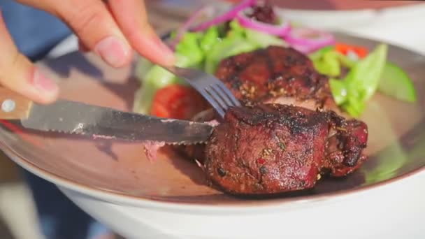 Крупным планом режут сочное свежее мясо на тарелке. Мужские руки отрезали кусок мяса на улице — стоковое видео