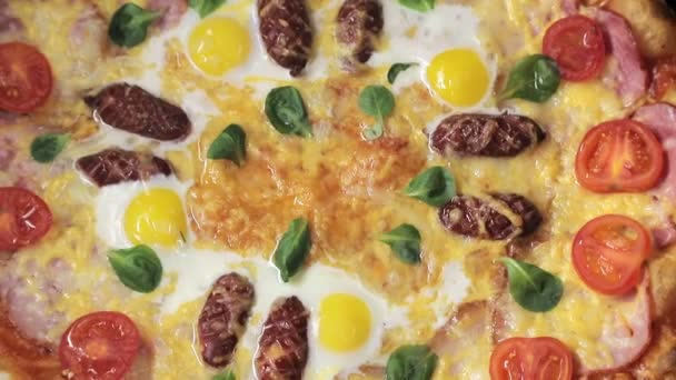 Крупным планом пицца с сырными помидорами, колбасой и яйцом, которая вращается вокруг себя, вид сверху — стоковое видео