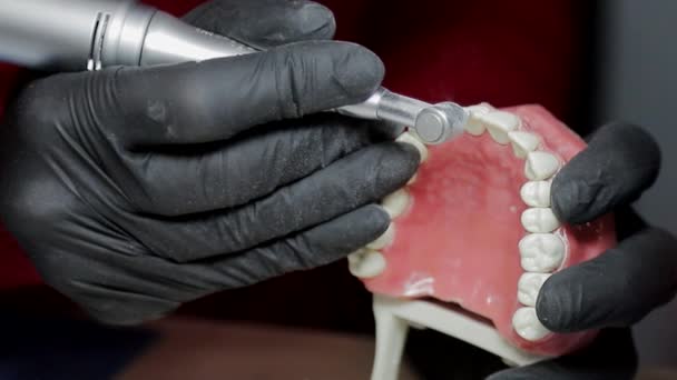 Dentista em luvas pretas Close-up de em um mock-up de um esqueleto de dentes usando uma máquina de broca. o dentista habilmente pratica alinhar os dentes da frente no layout — Vídeo de Stock