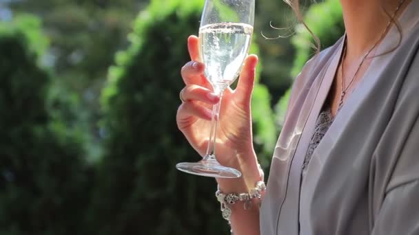 Ett glas champagne i flickornas hand. En stråle solljus lyser i ett glas champagne. Flickan dricker ur ett glas champagne — Stockvideo