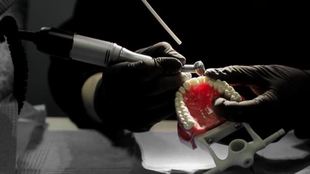 Close-up of a dentist practicing on a mock-up of a skeleton of teeth using a drill machine. the dentist deftly practices aligning the front teeth on the layout — Stock Video