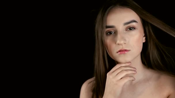 Chica de la moda con el pelo negro, morena gira la cabeza y balancea su cabello y efectivamente mira a la cámara. Modelo posando sobre un fondo negro — Vídeo de stock