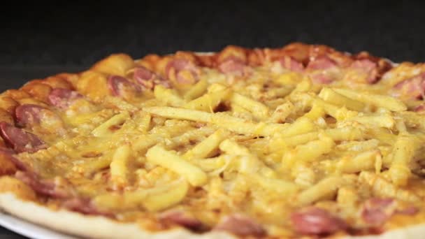 Nahaufnahme einer Pizza mit Käsetomaten, Wurst und Ei, die sich auf schwarzem Hintergrund von oben um sich selbst dreht — Stockvideo