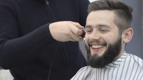 Corte de pelo en una peluquería. Barber le corta el pelo a sus maridos con un cortador. La sonrisa de un hombre que se corta el pelo — Vídeos de Stock