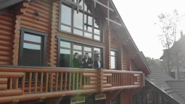 Drie zakenmannen in jassen schudden hand en knuffelen, ontmoeten elkaar op het balkon van het gebouw devellano — Stockvideo