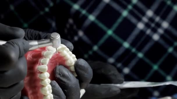 Dentista em luvas pretas Close-up de em um mock-up de um esqueleto de dentes usando uma máquina de broca. o dentista habilmente pratica alinhar os dentes da frente no layout — Vídeo de Stock