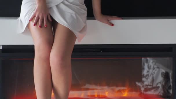 Beautiful legs of a girl on the background of a decorative fireplace in the room. Girl spiral on the fireplace and caresses your feet. — Stock Video