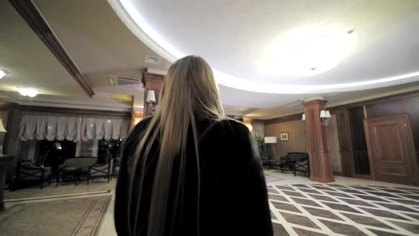 Die Geschäftsfrau verlässt das Hotel. Ein junges hübsches Mädchen geht durch die Hotellobby. Schießen von hinten — Stockvideo