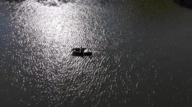 Gelinlerin hava görüntüsü kırmızı bir teknede yüzüyor. Parlak güneş göle yansıyor. Yansıma yapıyor ve parıldıyor..