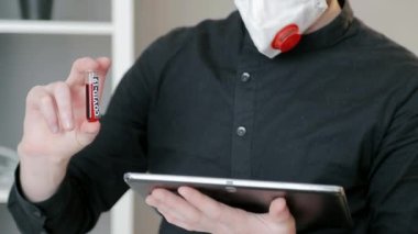 Doktorun elindeki coved19 virüsünün kan testiyle test tüpünün yakın çekimi. Doktor elinde bir kan testi tüpü ve tablet tutuyor..