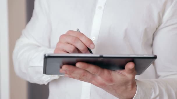 Close-up of a businessmans hand holding a stylus in his hand and working on a tablet — Stock Video
