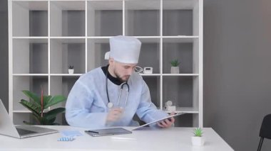 Ofiste çalışan doktor tabletteki bilgilere bakar ve metni bir sayfa kağıda yazar.
