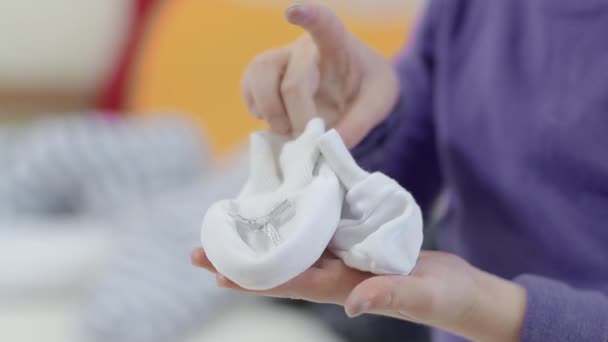 As mãos das crianças seguram pequenos sapatos brancos para o bebê no dia do Batismo . — Vídeo de Stock