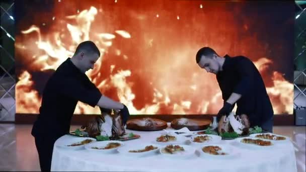 Οι σεφ κόβουν φρεσκοψημένο κρέας στο φόντο μιας μεγάλης οθόνης με τεχνητή φωτιά. Περιβάλλον ντίσκο. Φως από διαφορετικά χρώματα φωτίζει τη σκηνή. — Αρχείο Βίντεο