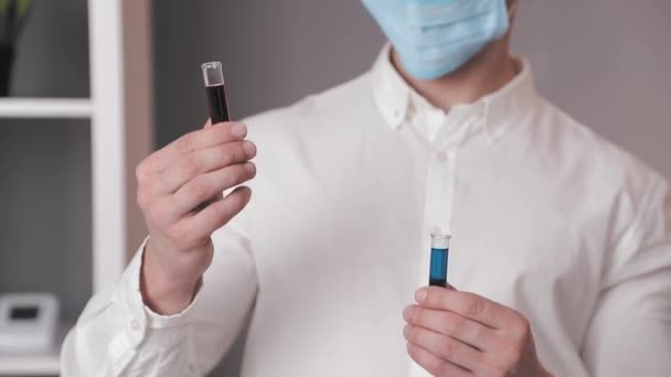 Il medico di laboratorio da vicino tiene due provette di colore rosso e blu ed le esamina. Il medico esamina le provette di laboratorio . — Video Stock