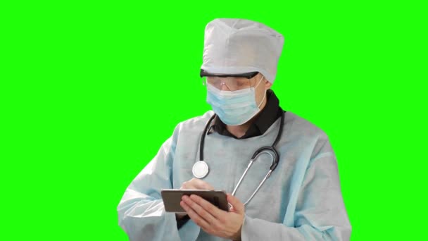 Young doctor in medical mask and protective medical clothing working in mobile phone. Shot on the background of Chrome Key. Chrome Kay high quality — Stock Video