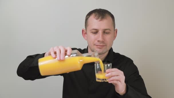 Чоловік вливає апельсиновий сік у склянку. Чоловік бере ковток апельсинового соку з щасливими емоціями — стокове відео