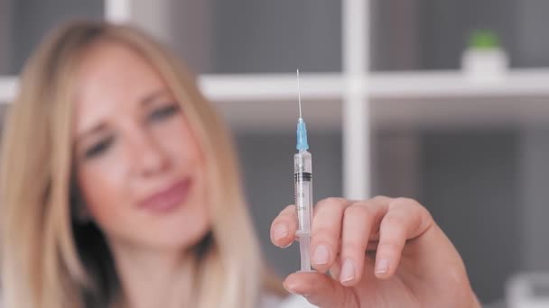 Doctor a woman of good appearance holds a syringe in her hand and releases excess air from the syringe and looks at the camera — Stock Video