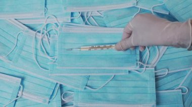 Hemşireler tıbbi eldiven veriyor. Sıcaklığı 38 derece olan bir termometre, tıbbi maske takıyor..