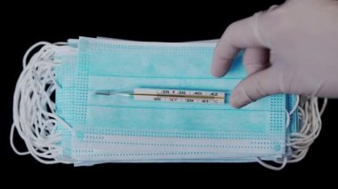 Doktor, tıbbi maskeye 38 derece sıcaklıkta bir termometre koydu. Doktor elinde bir termometre tutuyor ve tıbbi bir maske takıyor. Yüksek vücut sıcaklığı.