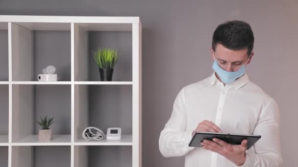 Lékař v ochranné lékařské masce pracuje na tabletu ve své kanceláři. — Stock video