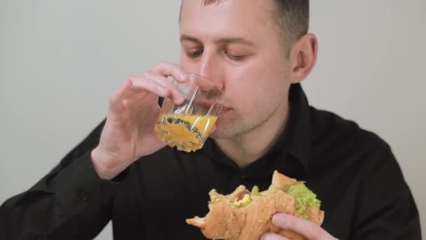 El hombre bebe jugo de naranja y come un delicioso bollo con verduras frescas y hierbas . — Vídeos de Stock