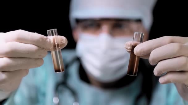 Close up An employee of Tims laboratory took two test tubes with various studies. Laboratory assistant examines the blood in test tubes. On black background — Stock Video