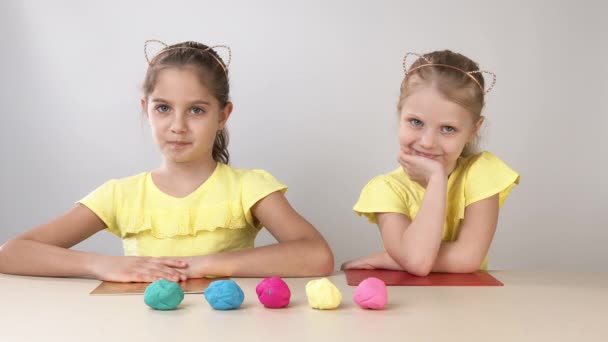 Des émotions heureuses de deux enfants. Deux petites filles soeurs jouant du plastelinom assises à la table. L'enfant joue avec la plasticine. Créativité des enfants . — Video