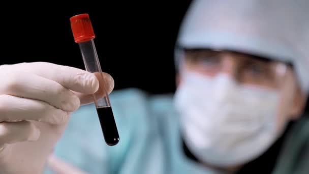 Close up Medical doctor performs a blood test. The technician holds a tube with a blood test in his hand and examines the blood. on black background. — Stock Video