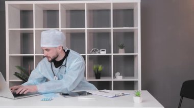Bilgisayarın ofisindeki işyerinde çalışan bir doktor. Tıbbi giysiler içinde bir doktor bilgisayarda daktilo yazıyor..