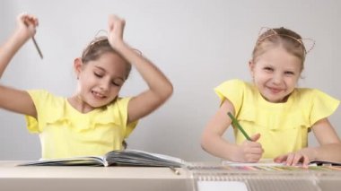 Komik ve komik çocuklar. Masadaki çocuklar dans edip yaratıyorlar. İki çocuk bir masada oturuyor ve boyama kitabı boyuyorlar..