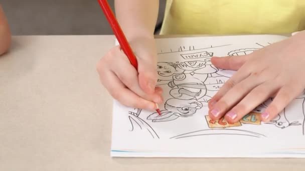 Una ragazza dipinge un libro da colorare. Primo piano di una mano di bambine che tiene una matita e un disegno . — Video Stock