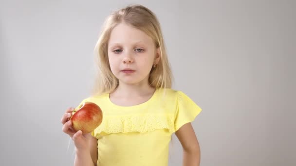 Chica con una manzana. Niña comiendo una Apple Girl en un vestido amarillo brillante sobre un fondo blanco . — Vídeos de Stock