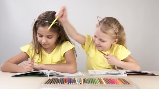 Niños divertidos y divertidos. Los niños en la mesa bailan y crean. Dos niños están sentados en una mesa y colorean un libro para colorear . — Vídeo de stock
