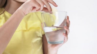 Küçük kız, suda çözünen vitaminlerle dolu bir tablet atıyor. Kız köpüklü ilaç içiyor..