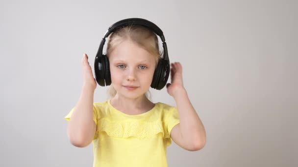 Ευτυχισμένα συναισθήματα ενός μικρού κοριτσιού με ένα φωτεινό κίτρινο φόρεμα. Ένα κοριτσάκι με ακουστικά που χορεύει και χαλαρώνει — Αρχείο Βίντεο