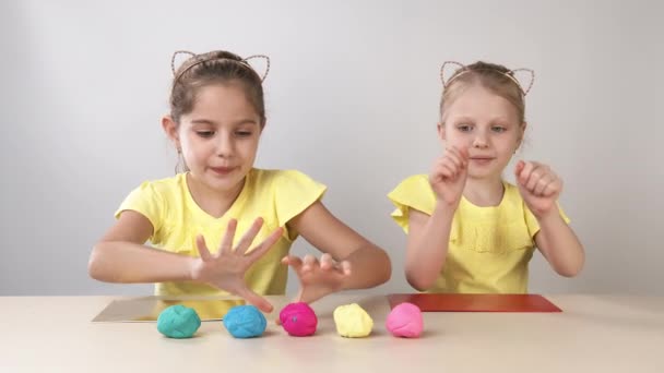 Creatividad infantil. Dos hermanas niñas jugando al plastelinom sentadas a la mesa. El niño jugando con plastilina — Vídeo de stock