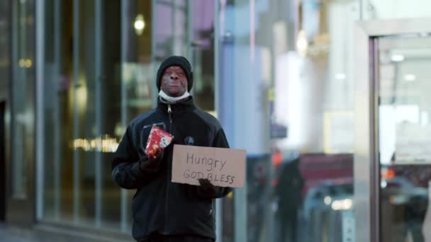 New York, États-Unis - Le 14 avril 2020 Un Noir debout à Times Square à Manhattan, tenant un panneau "Que Dieu bénisse la faim" et mangeant — Video