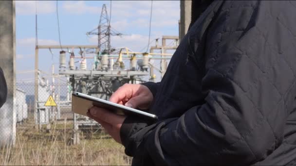Elektrik mühendisleri yüksek voltajlı bir elektrik santralinin tabletine veri giriyorlar. Bir adam elektrik trafo istasyonunun verilerini yazıyor. — Stok video