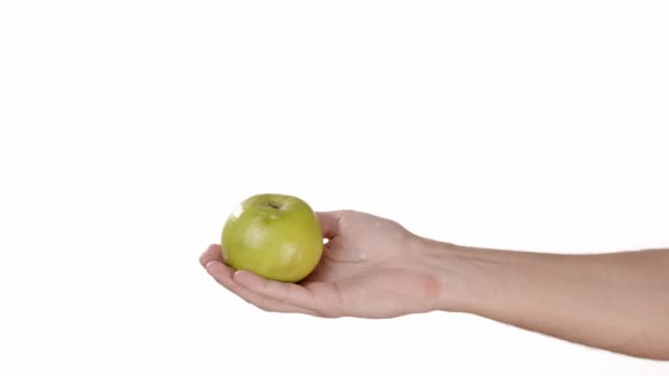 一只手放在白色的隔离背景上的男人拿着一个绿色的苹果扔在那里。插入文本或背景的位置。一个人的情感传递的背景是白色的. — 图库视频影像