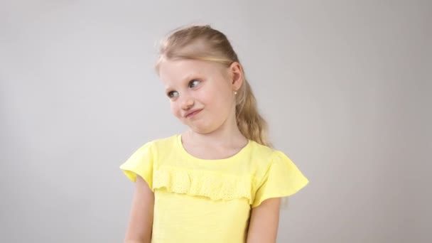 Las emociones de una niña. Retrato de una niña con un vestido amarillo sobre un fondo blanco . — Vídeos de Stock