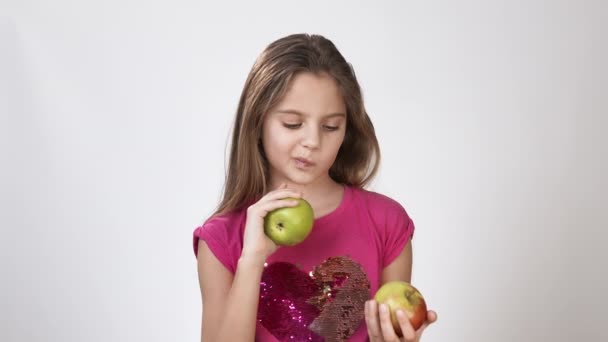 Chica con una manzana. niña sostiene una manzana en la mano y mira a la manzana. Chica en un vestido rosa brillante sobre un fondo blanco . — Vídeos de Stock