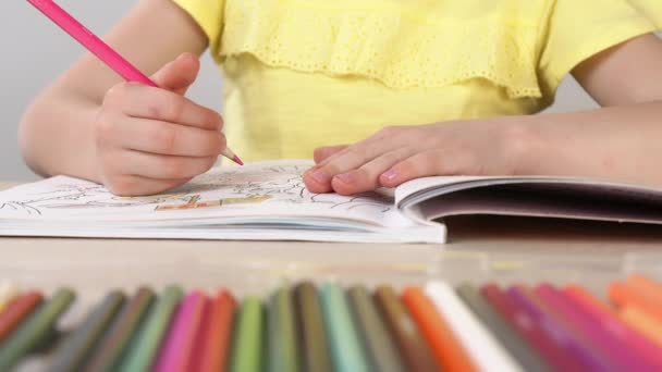 A girl paints a coloring book. Close-up of a little girls hand holding a pencil and drawing. — Stock Video