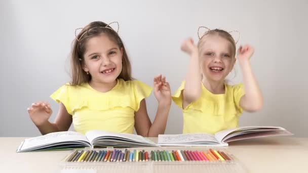 Lustige und lustige Kinder. Kinder am Tisch tanzen und basteln. Zwei Kinder sitzen an einem Tisch und malen ein Malbuch. — Stockvideo