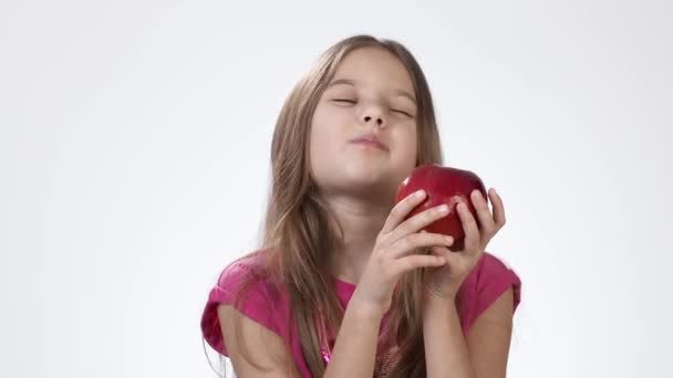 La niña de blanco se come una manzana roja grande. Una chica muerde un trozo de ceniza roja y lo prueba. . — Vídeo de stock