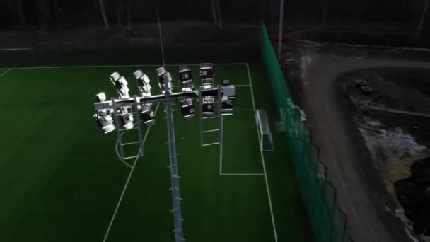 Campo de futebol que é iluminado na noite. Voando sobre dispositivos iluminados que iluminam o campo de futebol . — Vídeo de Stock