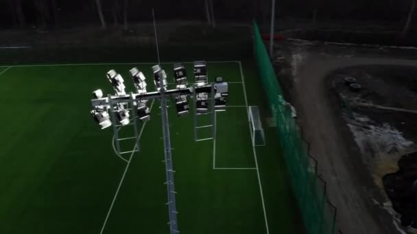 Gecenin karanlığında parlayan futbol sahası. Futbol sahasını aydınlatan aydınlatma cihazlarının üzerinde uçmak. — Stok video