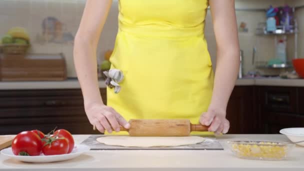 Γυναίκα σεφ μαγειρεύει στην κουζίνα με κίτρινα ρούχα. Γυναικεία χέρια λειαίνουν τη ζύμη στο τραπέζι της πίτσας. — Αρχείο Βίντεο